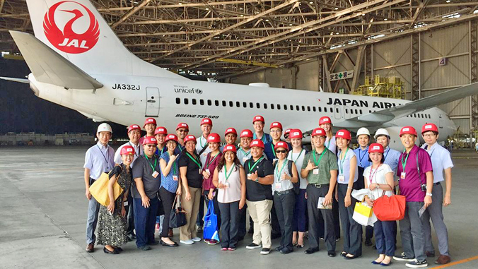 large group of people wearing red caps standing in front of a Japan Airlines plane