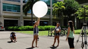 student holding on to white weather balloon
