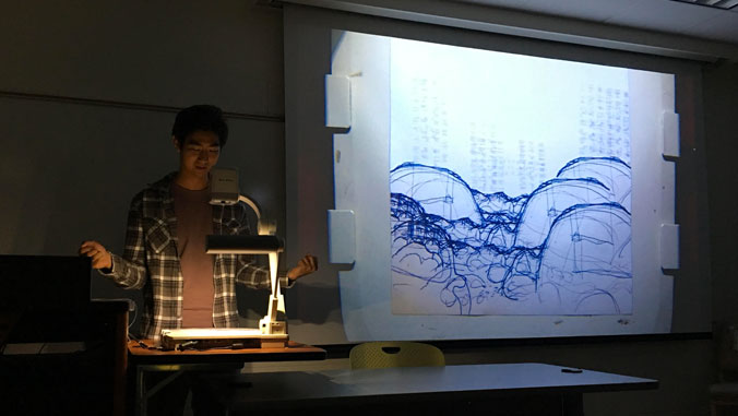 Student presents drawing in darkened classroom.