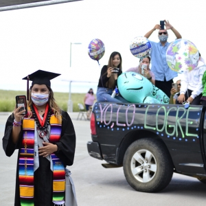 student graduate with family behind in car