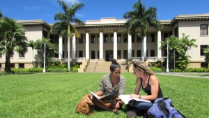 two people sitting down on grass looking at a book
