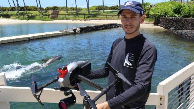man holding drone with dolphin in background