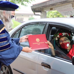chancellor handing graduate a diploma in a car