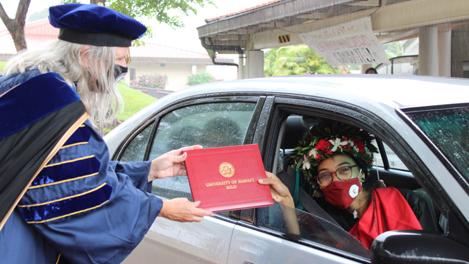 chancellor handing graduate a diploma in a car