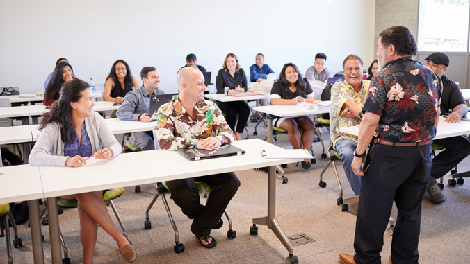 person standing talking to several people seated with desks