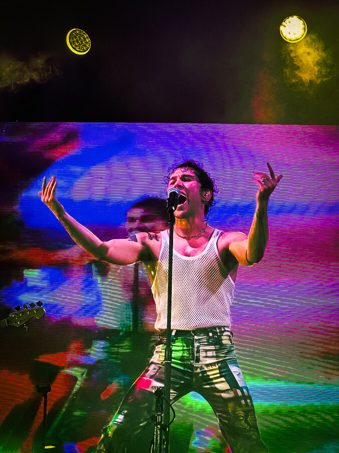 MAX singing into a microphone with a neon backdrop