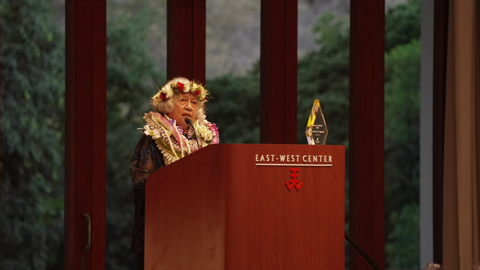 person with lei standing at a podium with an award