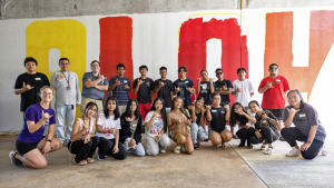 group of people posing in front of an ALOHA mural