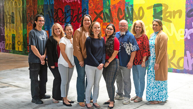 nine people standing in front of a mural