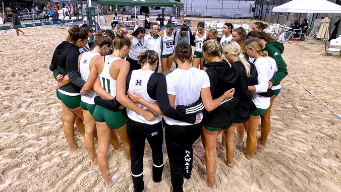 U H beach volleyball players in huddle on court