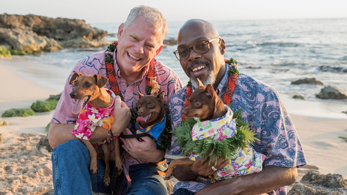 two people with aloha shirts and three dogs smiling