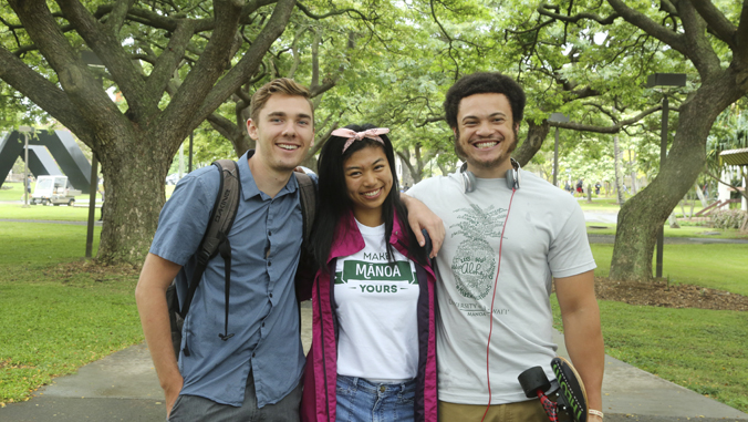 three people standing and smiling by a group of trees