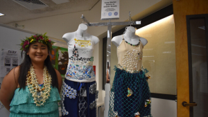 Student standing next to fashion designs
