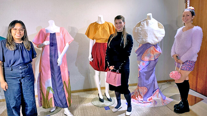 3 people standing next to 3 dresses on mannequins