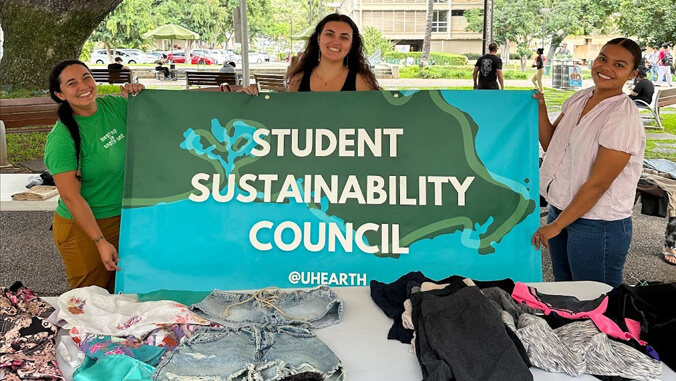 three students hold a student sustainability council banner at clothing swap