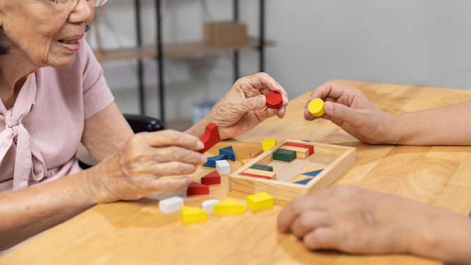 Caregiver and senior woman playing wooden shape puzzles game for dementia prevention